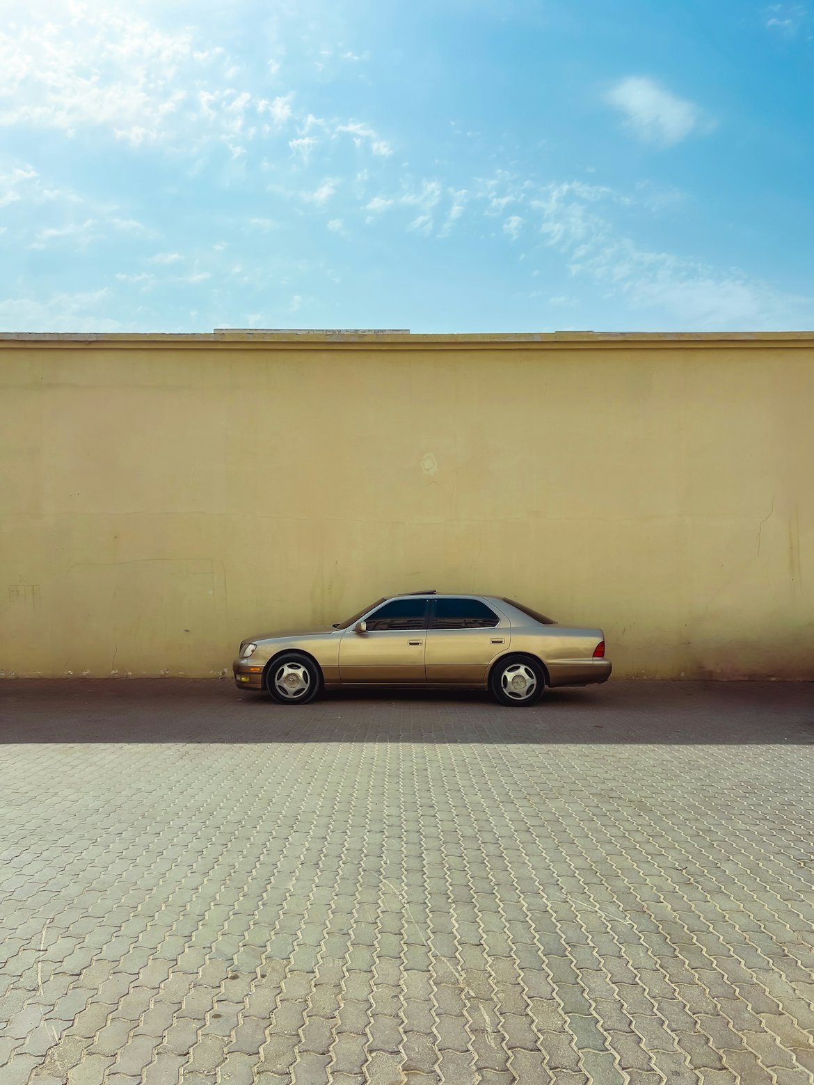 Une berline dorée garée au soleil devant un mur ocre